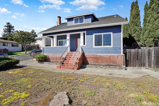 bungalow-style home with a chimney, fence, and brick siding