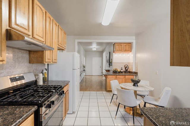 kitchen featuring light tile patterned floors, dark stone counters, decorative backsplash, gas range, and under cabinet range hood