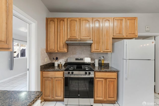 kitchen featuring tasteful backsplash, dark stone countertops, freestanding refrigerator, stainless steel gas range, and under cabinet range hood