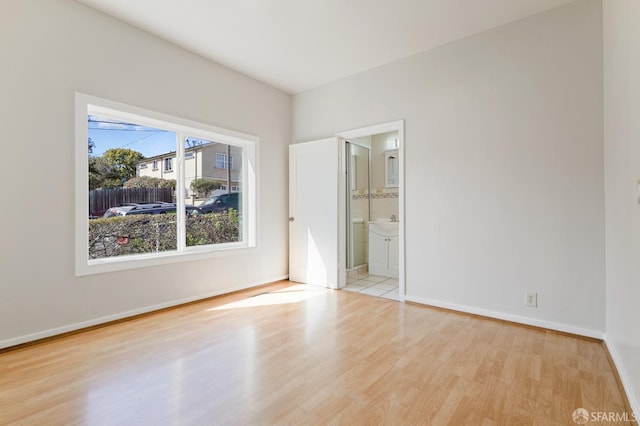 unfurnished bedroom featuring ensuite bath, baseboards, and wood finished floors