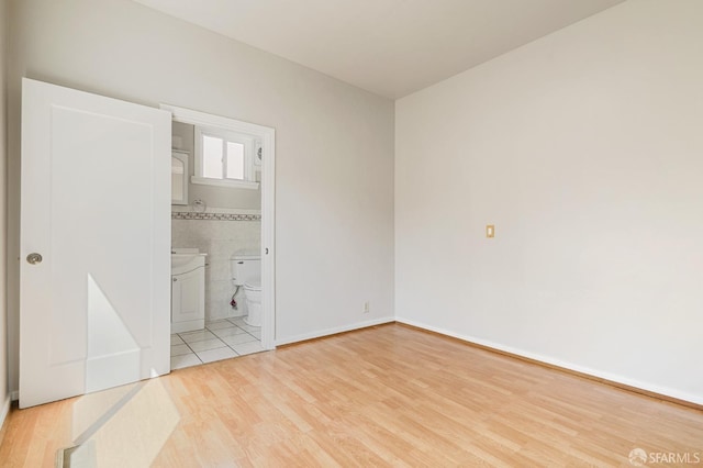 unfurnished bedroom featuring ensuite bath, light wood-style flooring, and tile walls