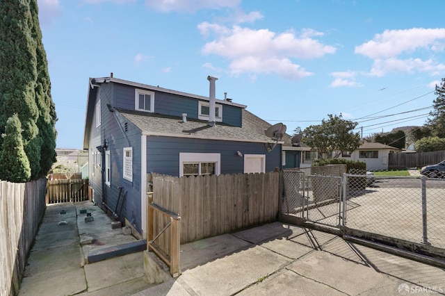 rear view of property featuring a shingled roof, fence, and a gate