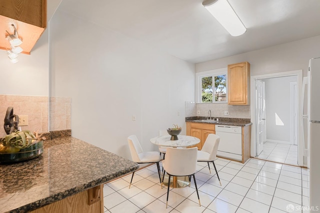 kitchen with white appliances, light tile patterned floors, dark countertops, a sink, and backsplash