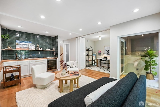 living area with beverage cooler, light wood finished floors, recessed lighting, stairs, and bar area