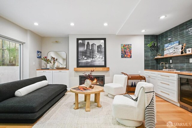 living room with light wood-style flooring, a glass covered fireplace, recessed lighting, wine cooler, and wet bar