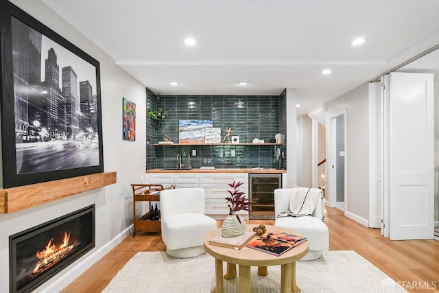 living room with beverage cooler, a warm lit fireplace, recessed lighting, light wood finished floors, and wet bar