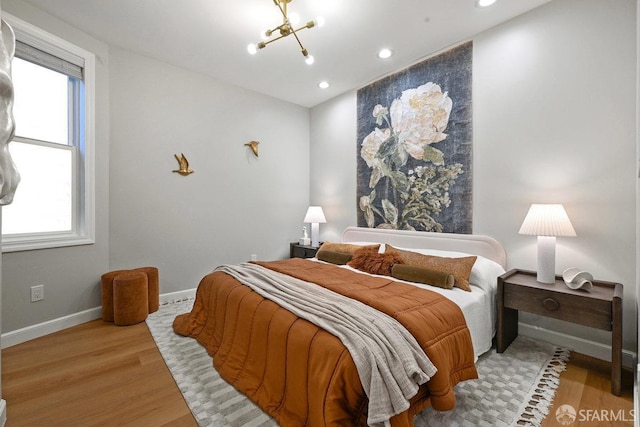 bedroom featuring baseboards, multiple windows, wood finished floors, and a chandelier