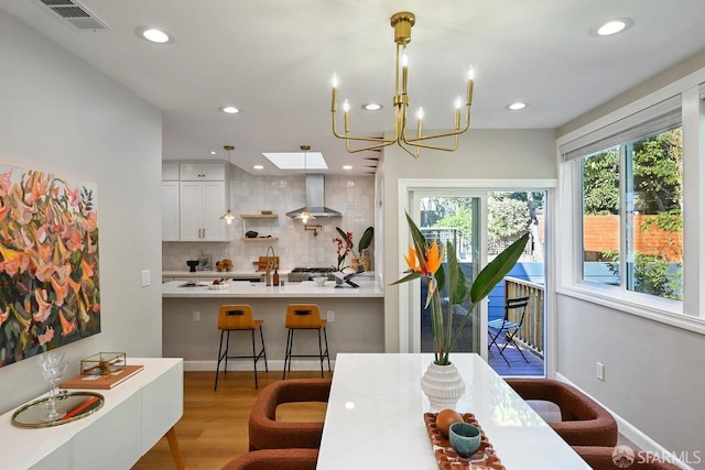 dining room featuring light wood-type flooring, visible vents, recessed lighting, a skylight, and baseboards