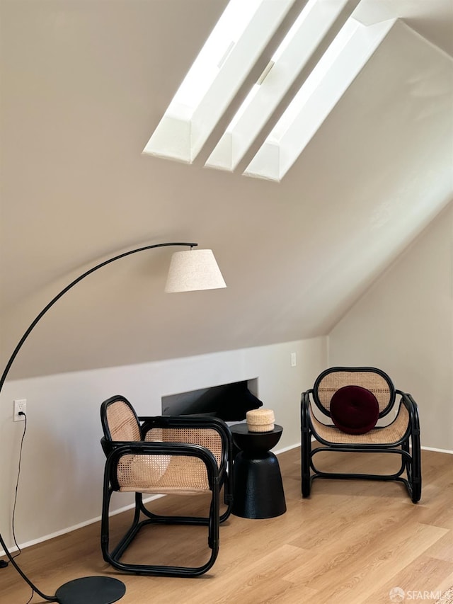 living area featuring baseboards, vaulted ceiling with skylight, and wood finished floors