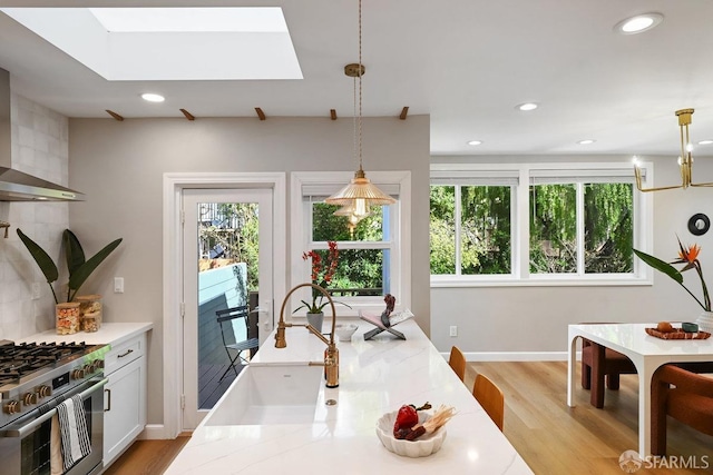 kitchen with light wood-type flooring, high end stainless steel range oven, wall chimney range hood, recessed lighting, and light countertops