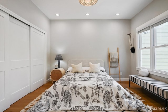 bedroom with recessed lighting, wood finished floors, baseboards, and a closet