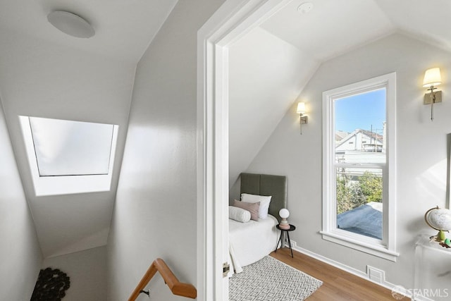 bedroom featuring lofted ceiling with skylight, baseboards, and wood finished floors