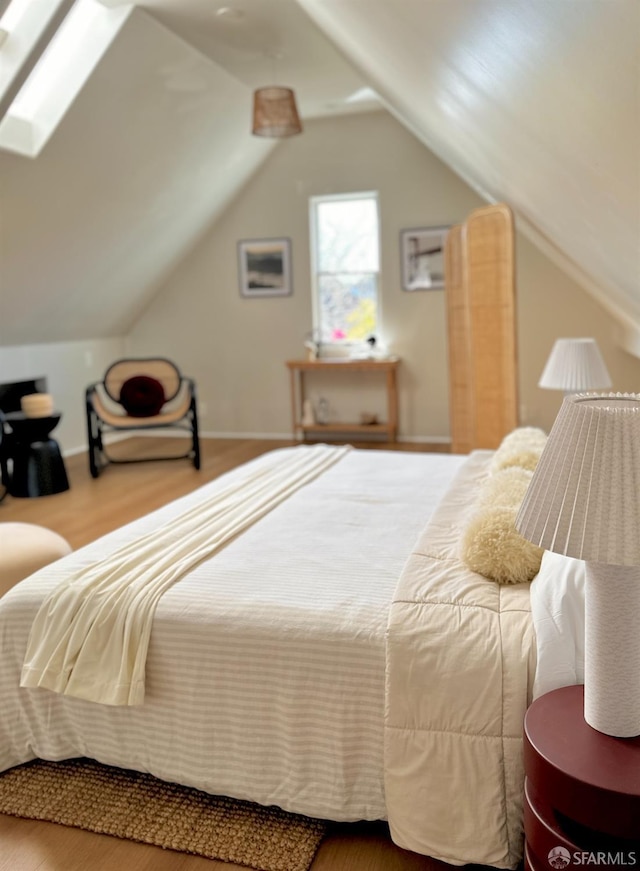 bedroom with vaulted ceiling with skylight and wood finished floors