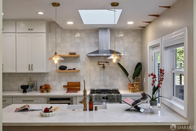 kitchen featuring light stone counters, appliances with stainless steel finishes, a skylight, white cabinets, and wall chimney exhaust hood