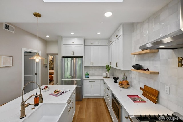 kitchen featuring tasteful backsplash, visible vents, freestanding refrigerator, wall chimney exhaust hood, and a sink