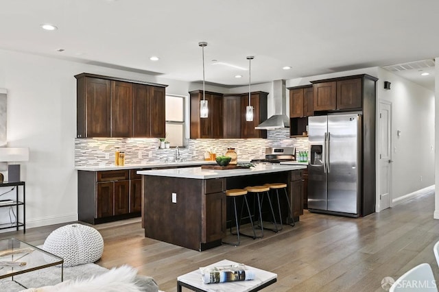 kitchen with light wood-style floors, wall chimney range hood, appliances with stainless steel finishes, and visible vents