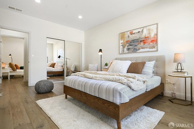bedroom with recessed lighting, wood finished floors, visible vents, a closet, and baseboards