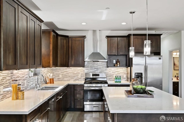 kitchen with stainless steel appliances, wall chimney range hood, a sink, a kitchen island, and dark brown cabinetry