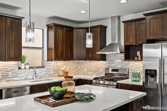 kitchen with dark brown cabinets, wall chimney range hood, a sink, tasteful backsplash, and appliances with stainless steel finishes