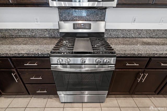 kitchen with dark brown cabinets, stainless steel range with gas cooktop, dark stone countertops, and light tile patterned flooring