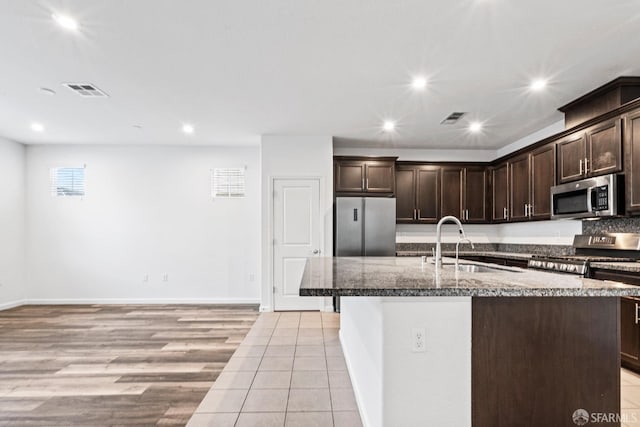 kitchen featuring dark brown cabinetry, sink, stainless steel appliances, an island with sink, and light hardwood / wood-style floors