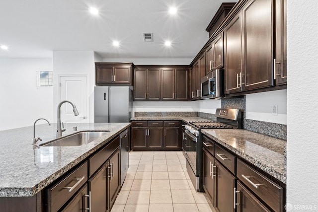 kitchen with sink, stainless steel appliances, an island with sink, dark brown cabinets, and light tile patterned floors