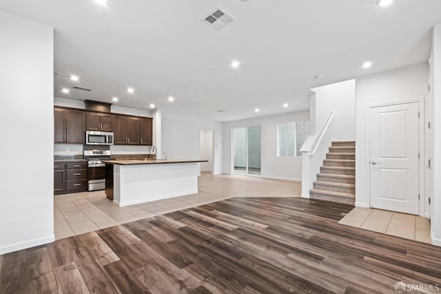 kitchen with dark brown cabinetry, an island with sink, stainless steel appliances, and light hardwood / wood-style floors