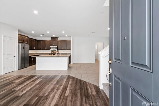 kitchen featuring a kitchen island with sink, dark brown cabinets, stainless steel appliances, and light hardwood / wood-style floors