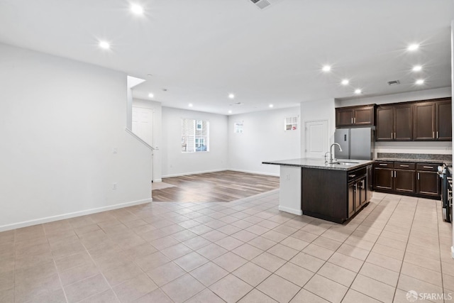 kitchen with dark brown cabinetry, sink, a center island with sink, light hardwood / wood-style floors, and stainless steel refrigerator