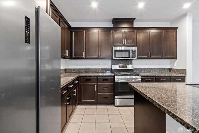 kitchen featuring dark brown cabinetry, light tile patterned floors, dark stone counters, and appliances with stainless steel finishes