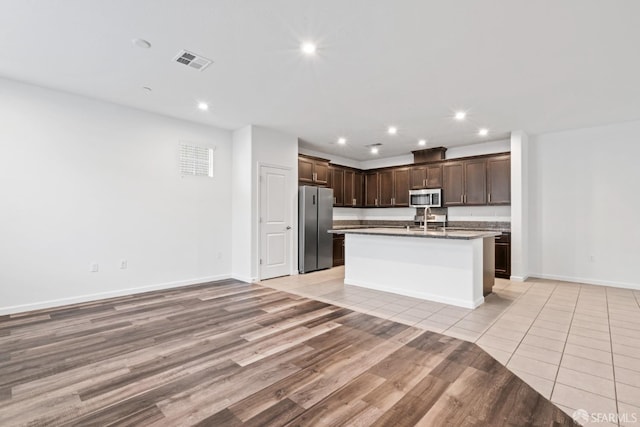 kitchen featuring sink, light wood-type flooring, an island with sink, dark brown cabinets, and stainless steel appliances