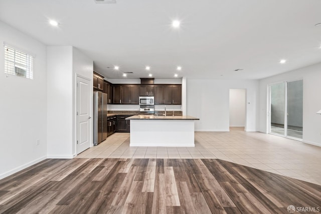 kitchen with dark brown cabinetry, stainless steel appliances, sink, a center island with sink, and light hardwood / wood-style floors