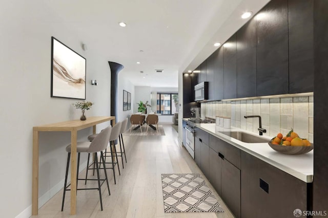 kitchen featuring white microwave, light countertops, decorative backsplash, high end range, and a sink