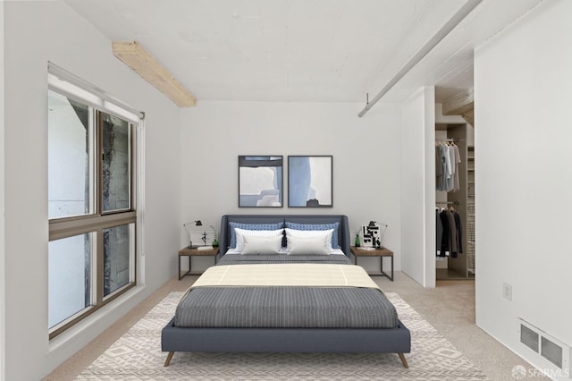 carpeted bedroom featuring beam ceiling and a walk in closet