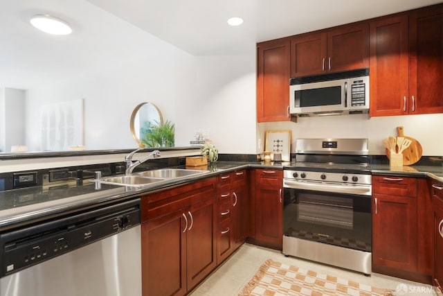 kitchen with recessed lighting, a sink, appliances with stainless steel finishes, reddish brown cabinets, and dark countertops