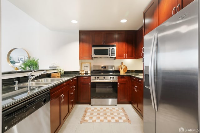 kitchen with stainless steel appliances, reddish brown cabinets, a sink, and dark countertops