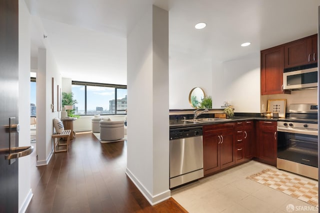 kitchen featuring dark countertops, appliances with stainless steel finishes, a sink, dark brown cabinets, and baseboards