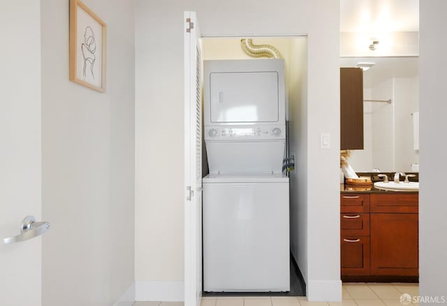 clothes washing area featuring laundry area, baseboards, stacked washer and clothes dryer, a sink, and light tile patterned flooring