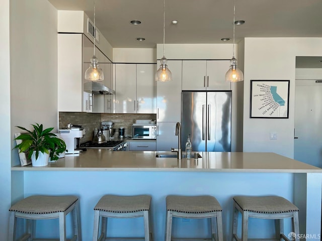 kitchen with white microwave, a peninsula, a sink, modern cabinets, and stainless steel fridge