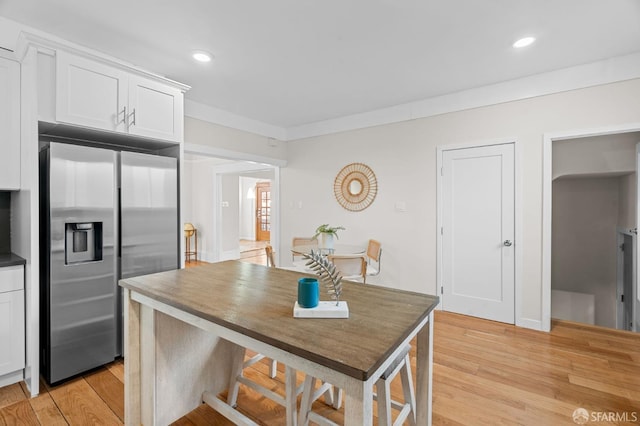 kitchen with crown molding, white cabinets, stainless steel fridge with ice dispenser, light hardwood / wood-style floors, and a breakfast bar area