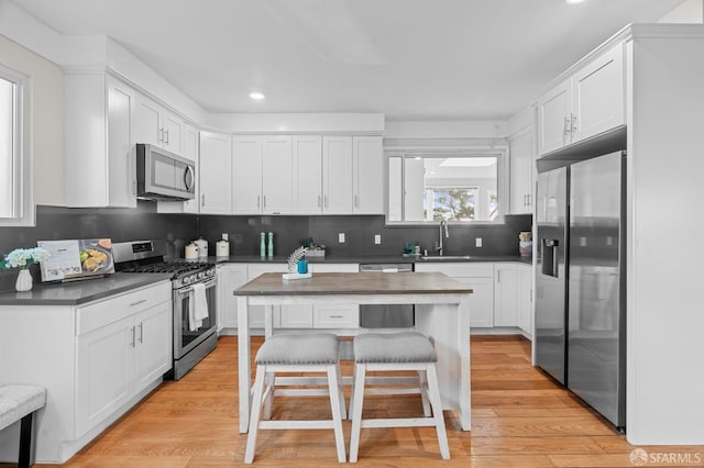 kitchen featuring a kitchen breakfast bar, tasteful backsplash, light hardwood / wood-style floors, white cabinets, and appliances with stainless steel finishes