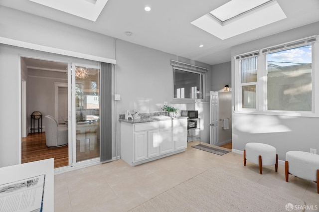 interior space with light tile patterned flooring, light stone counters, white cabinetry, and a skylight