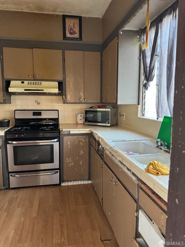 kitchen featuring hardwood / wood-style floors, tile counters, decorative backsplash, appliances with stainless steel finishes, and exhaust hood