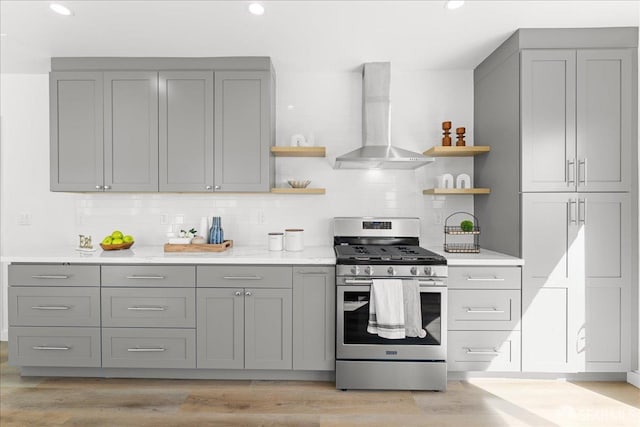 kitchen with wall chimney exhaust hood, gray cabinetry, open shelves, and stainless steel gas range oven