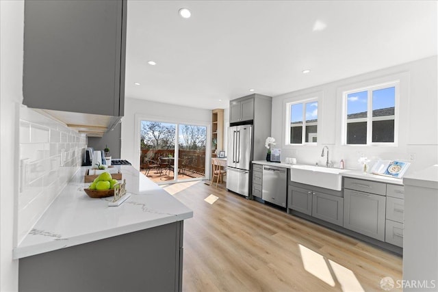 kitchen featuring stainless steel appliances, backsplash, gray cabinetry, a sink, and light wood-type flooring