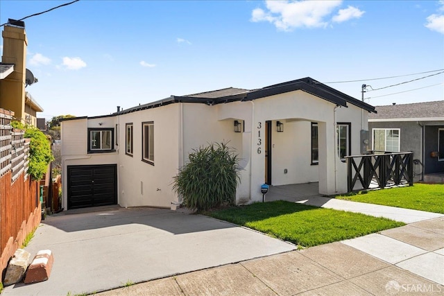 view of front of house with a front yard, concrete driveway, fence, and stucco siding