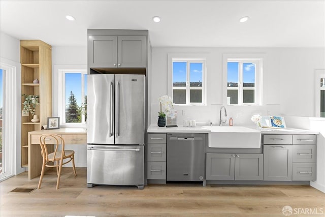 kitchen with a sink, stainless steel appliances, light wood-type flooring, and gray cabinets