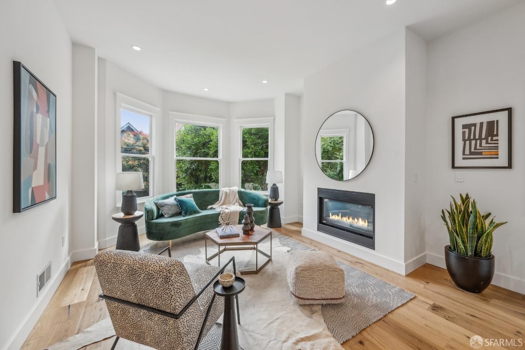 living area featuring a glass covered fireplace, wood finished floors, visible vents, and baseboards