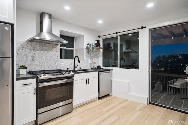 kitchen featuring light wood-style flooring, a sink, stainless steel appliances, dark countertops, and wall chimney exhaust hood