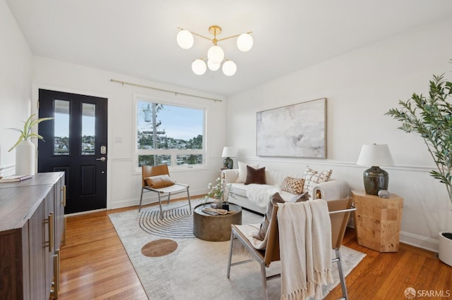 living room featuring an inviting chandelier, baseboards, and light wood finished floors